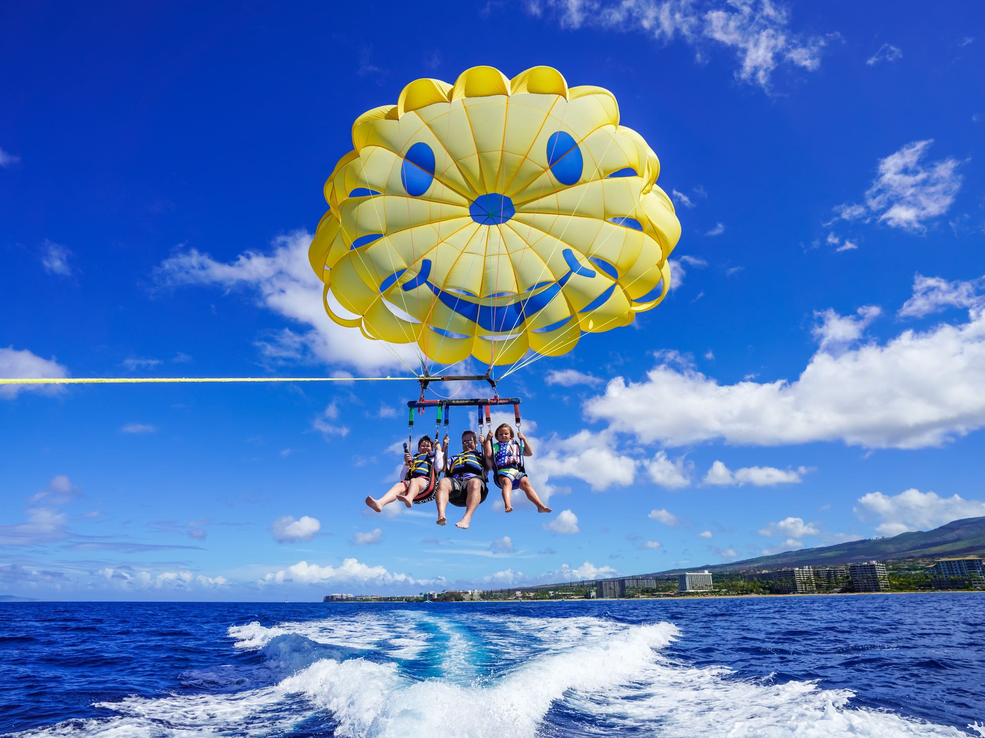 Three flyers under the yellow smiley canopy above Kāʻanapali Beach